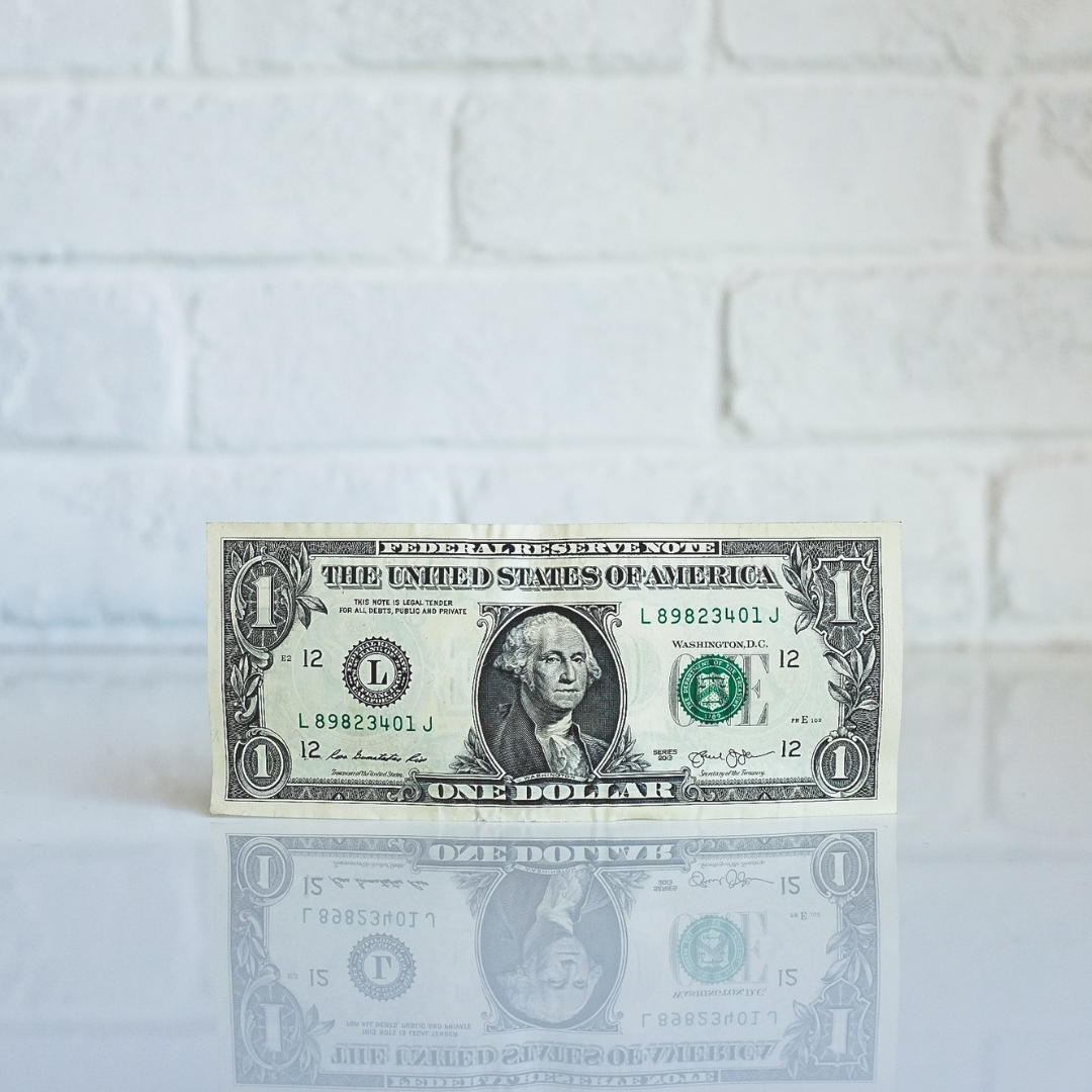 A dollar bill on a white table against a white brick wall.